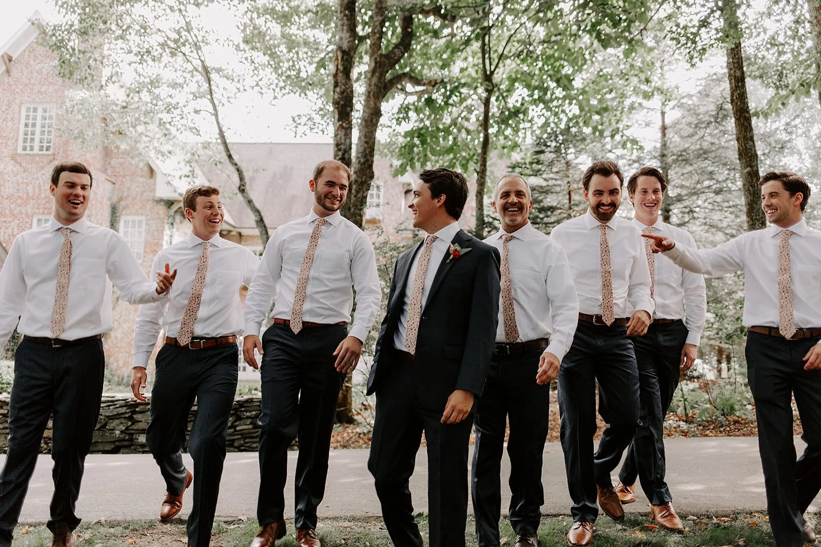 Groom and groomsmen walking outdoors in dress shirts, suspenders, and ties before the wedding ceremony.