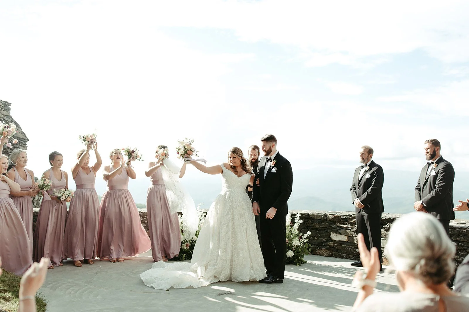 Bride and groom celebrating after the ceremony as the bridal party cheers at a mountain overlook.