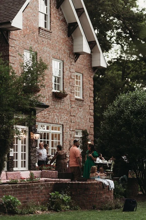 Guests mingle on the patio of a brick manor house during an outdoor wedding welcome party.