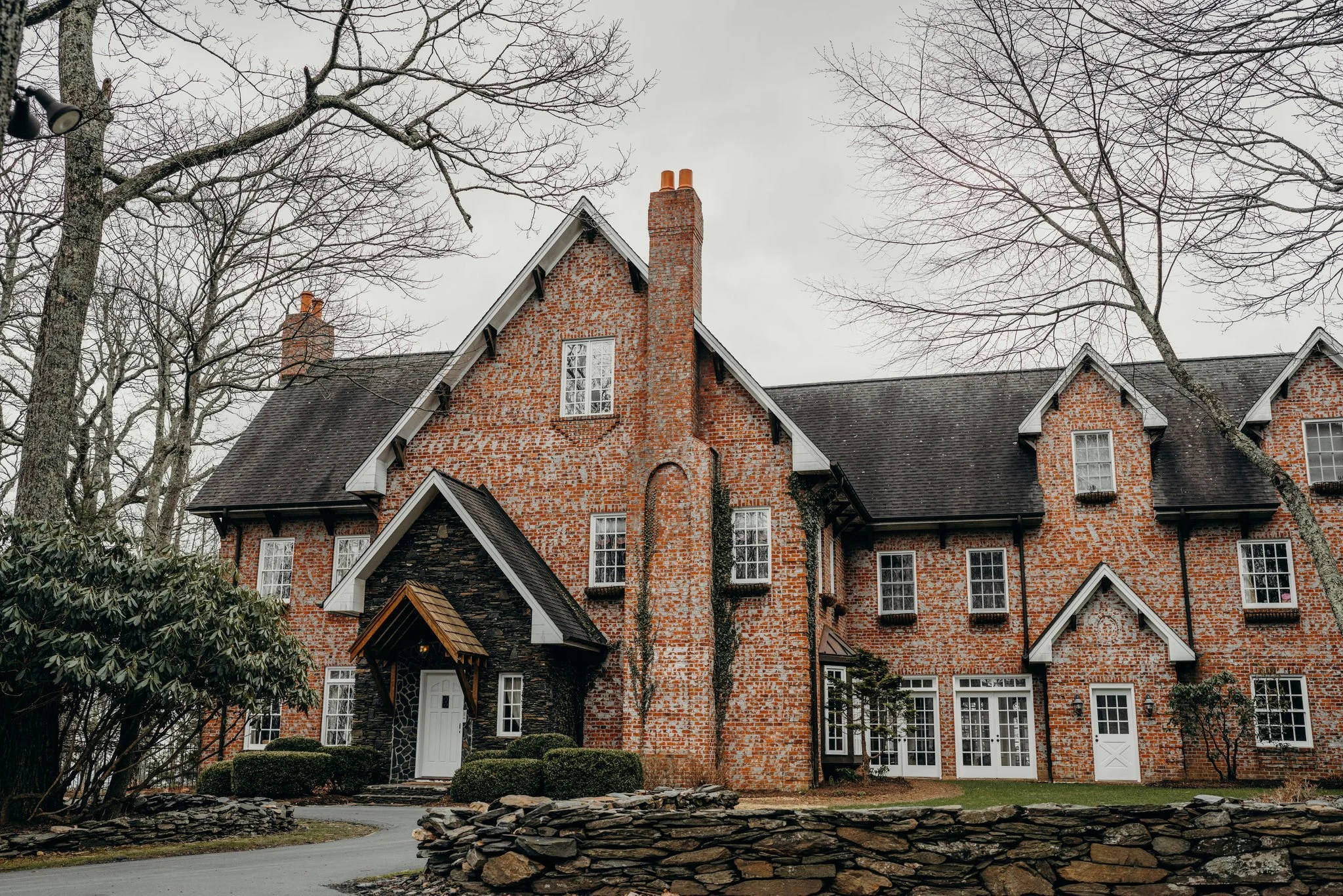 Exterior of a brick estate wedding venue with steep gables, chimneys, and bare trees on an overcast day