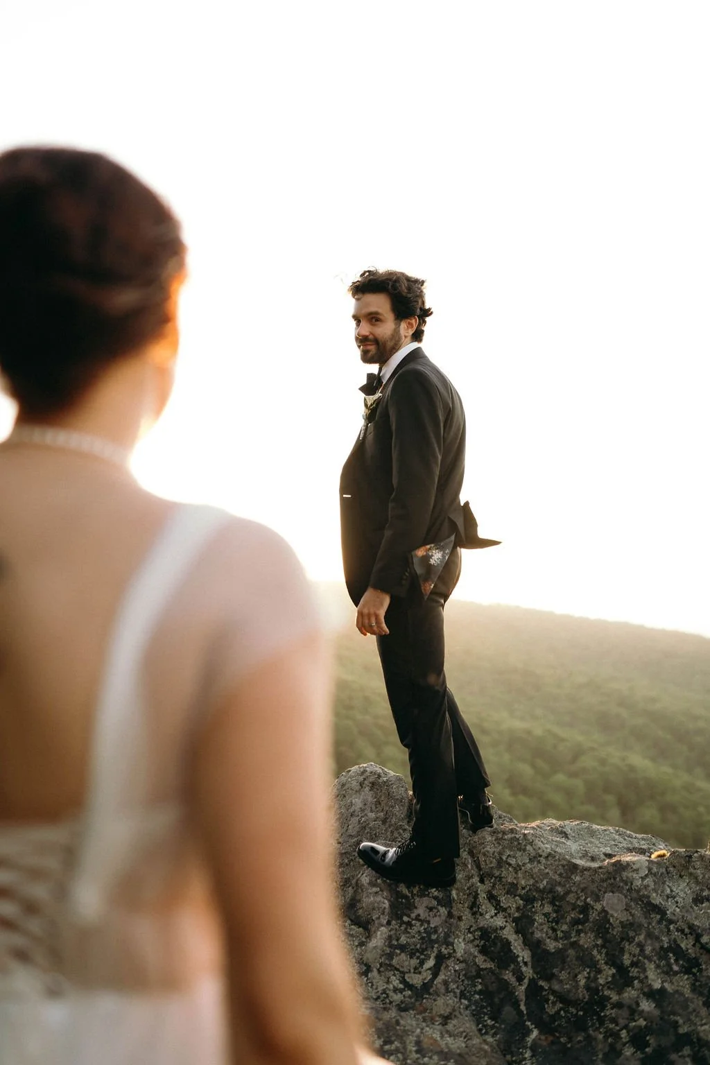 groom-on-rocky-mountain-cliff-with-bride-foreground.jpg