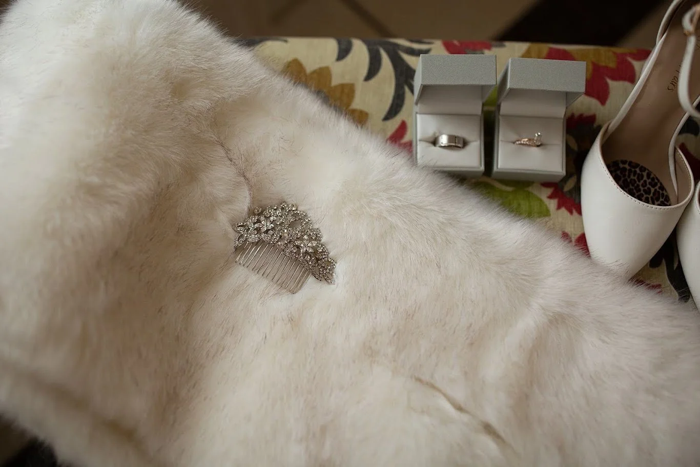 Bridal details flat lay with a fur wrap, rings in boxes, and a sparkling hair comb.