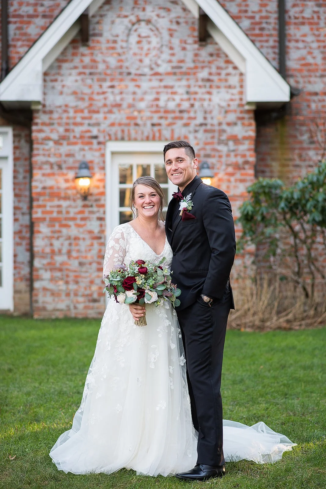 Bride and groom smiling together in front of a brick wedding venue during portraits.