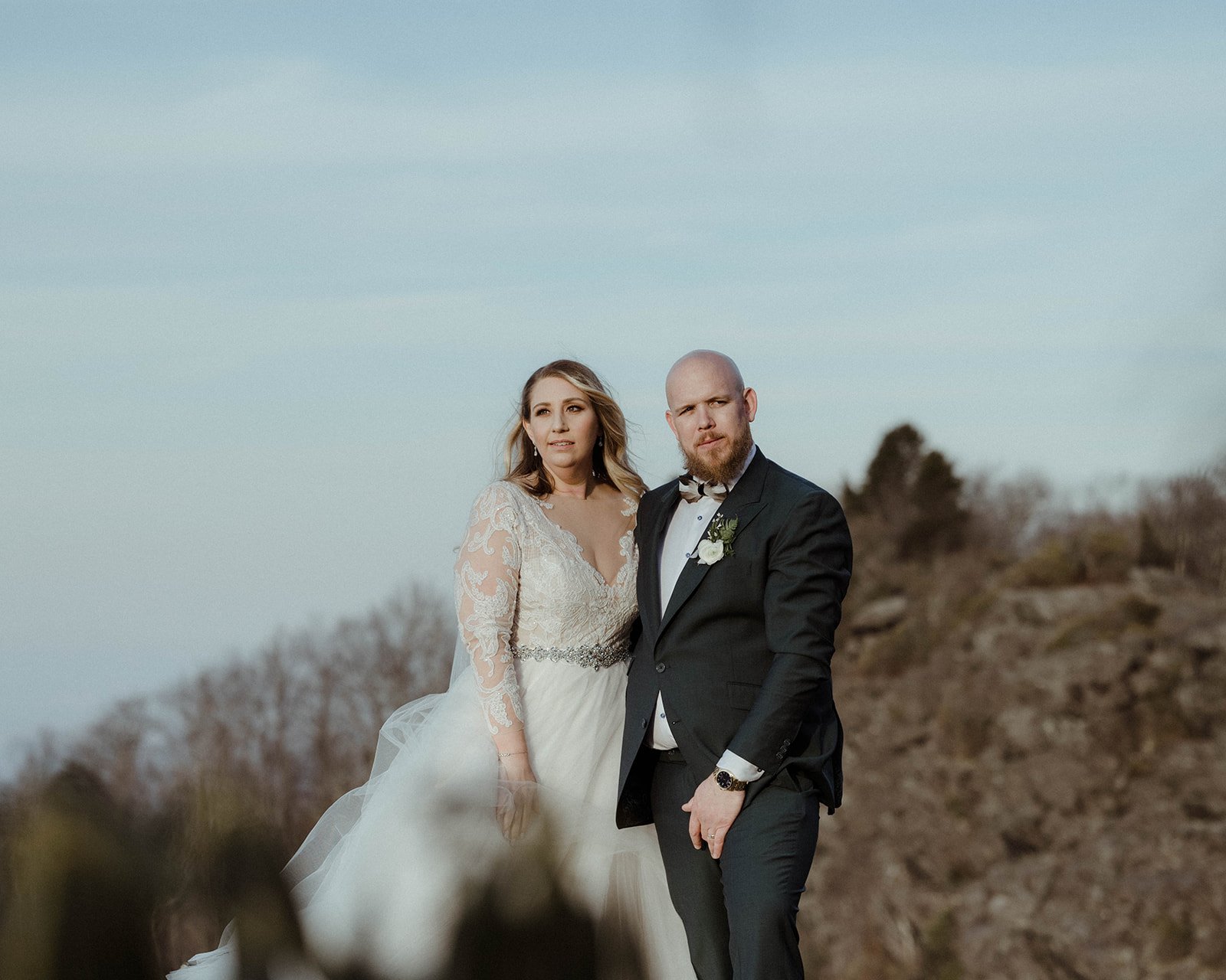 Bride and groom seated together on a rocky mountain overlook for a soft scenic wedding portrait.