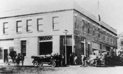 Black-and-white vintage photo of people gathered outside the hotel with an early automobile parked in front.