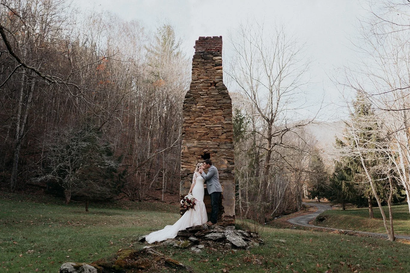 Bride and groom kissing beside a tall stone chimney at a mountain wedding venue