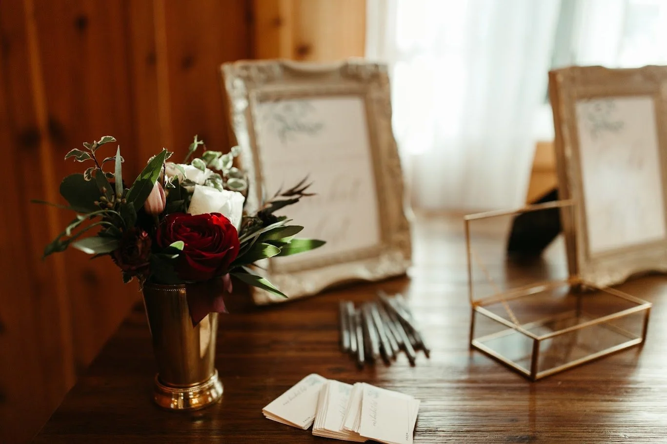 Framed wedding stationery and floral details displayed on a wooden table before the ceremony.