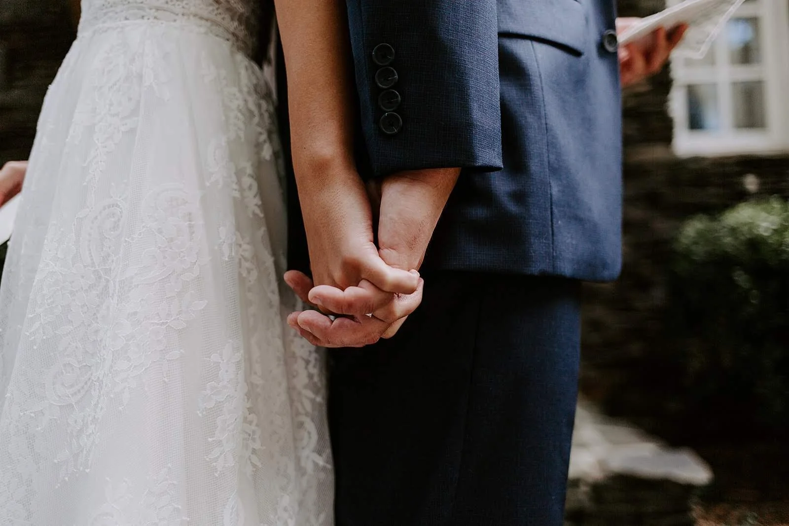 A close-up shows a bride in a white lace dress and a groom in a dark suit holding hands.