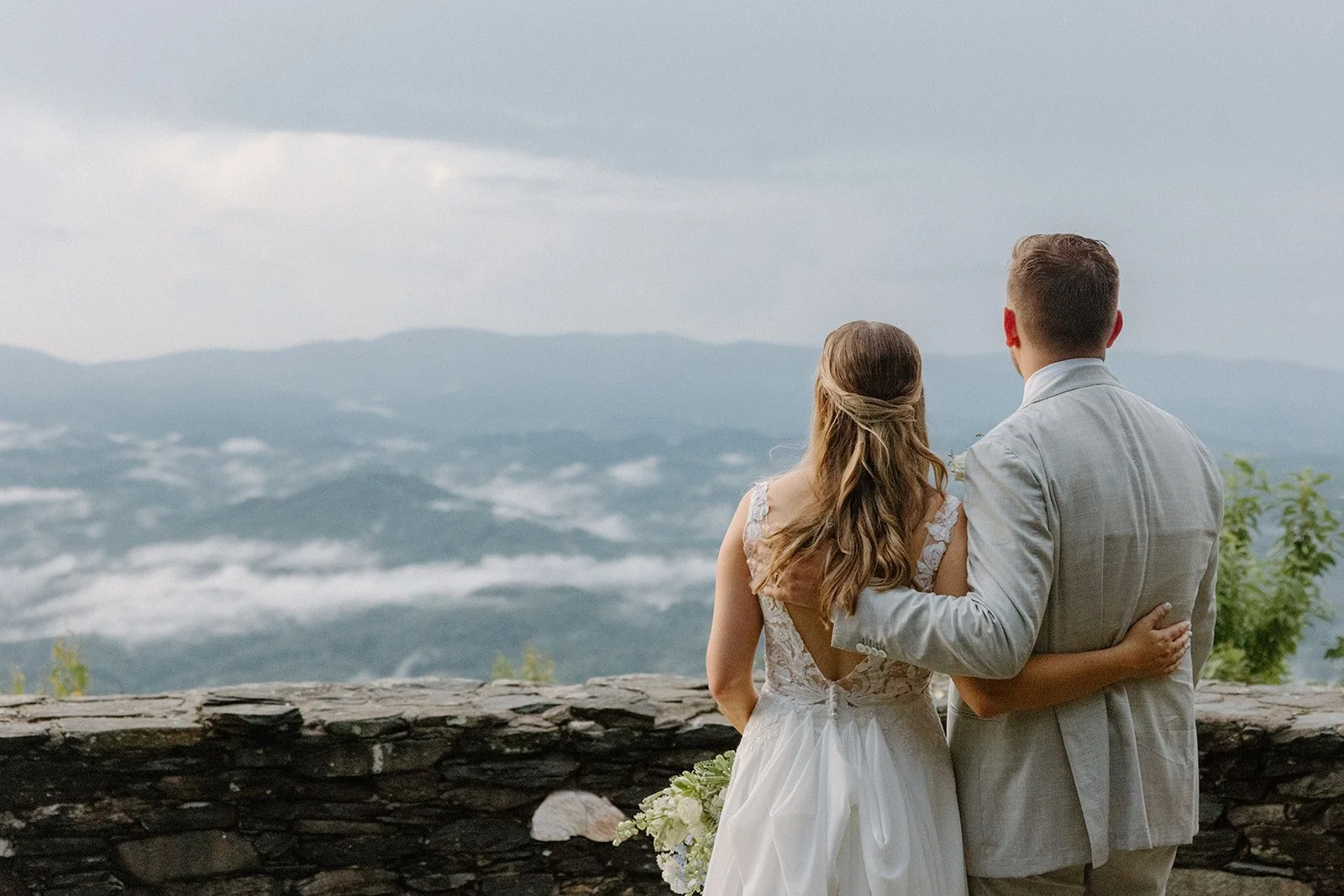 Newlyweds standing arm in arm overlooking misty Blue Ridge mountain views after their wedding ceremony