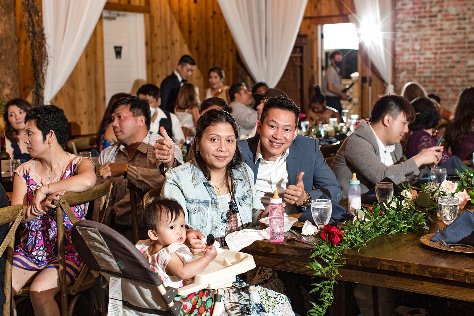 Wedding guests seated at a rustic reception table with greenery decor and family gathered together.