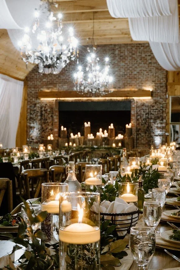 Close-up of a wedding reception table featuring floating candles in glass vases and greenery centerpieces.