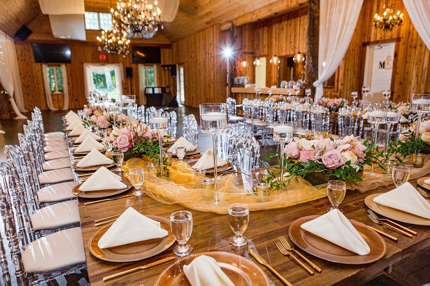Rustic barn wedding reception table with blush florals, greenery garland, and candle centerpieces