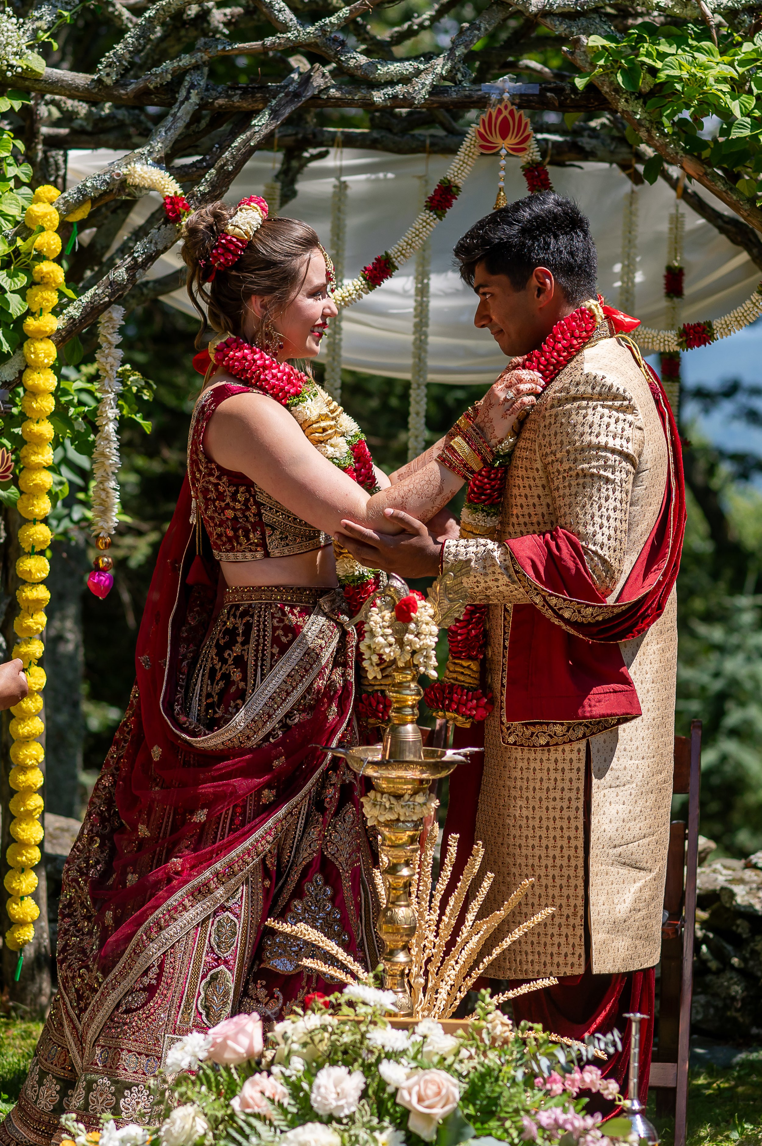 Bride and groom exchanging flower garlands during an outdoor Hindu wedding ceremony.