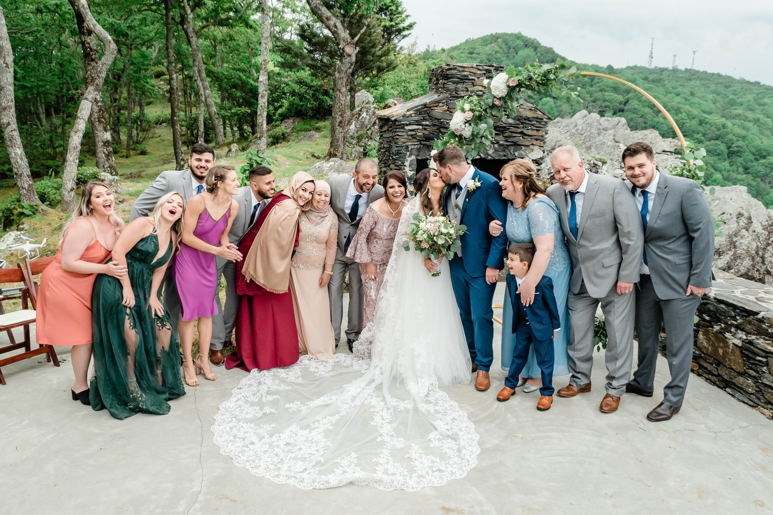 Wedding party group photo at a mountaintop ceremony with the bride’s long lace train spread out