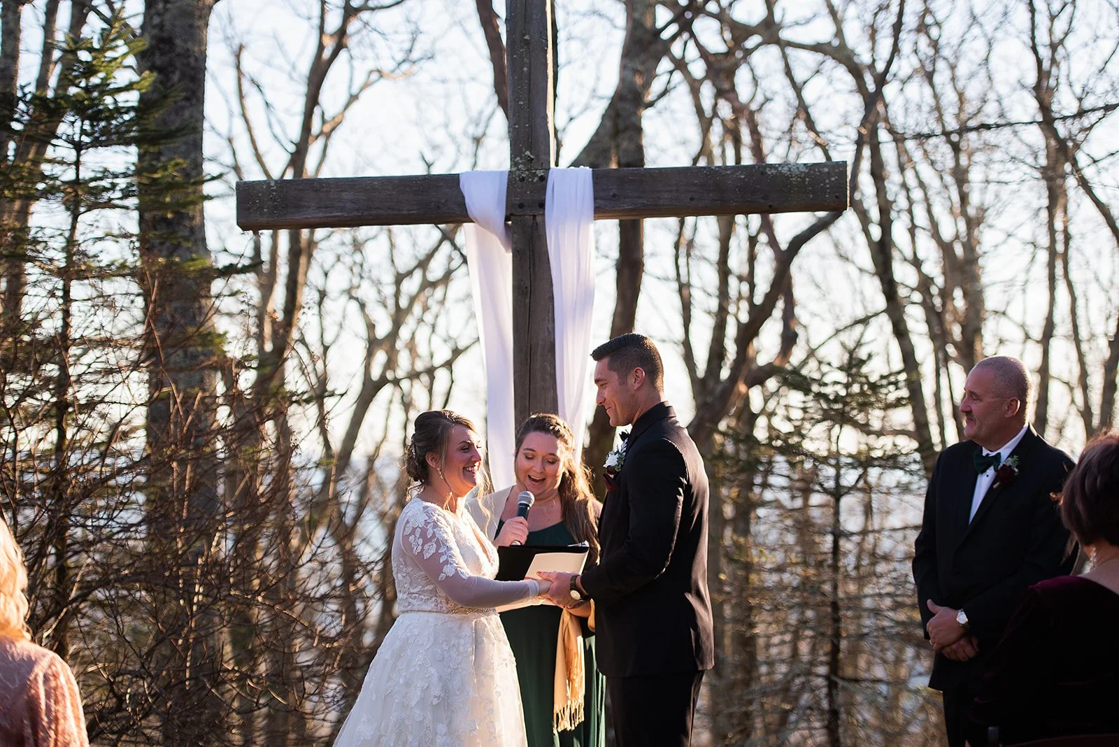 Couple exchanging vows under a wooden cross during an outdoor mountain wedding ceremony.