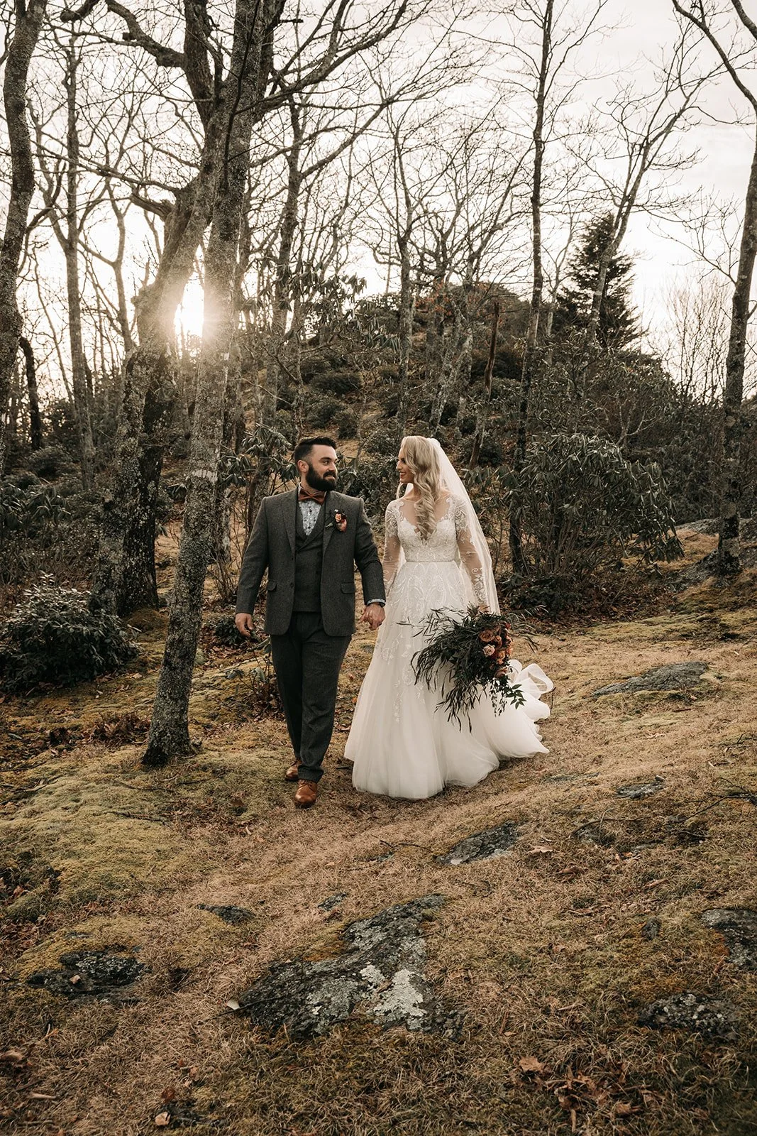 Bride and groom walking hand in hand through a wooded mountain trail after their wedding ceremony.