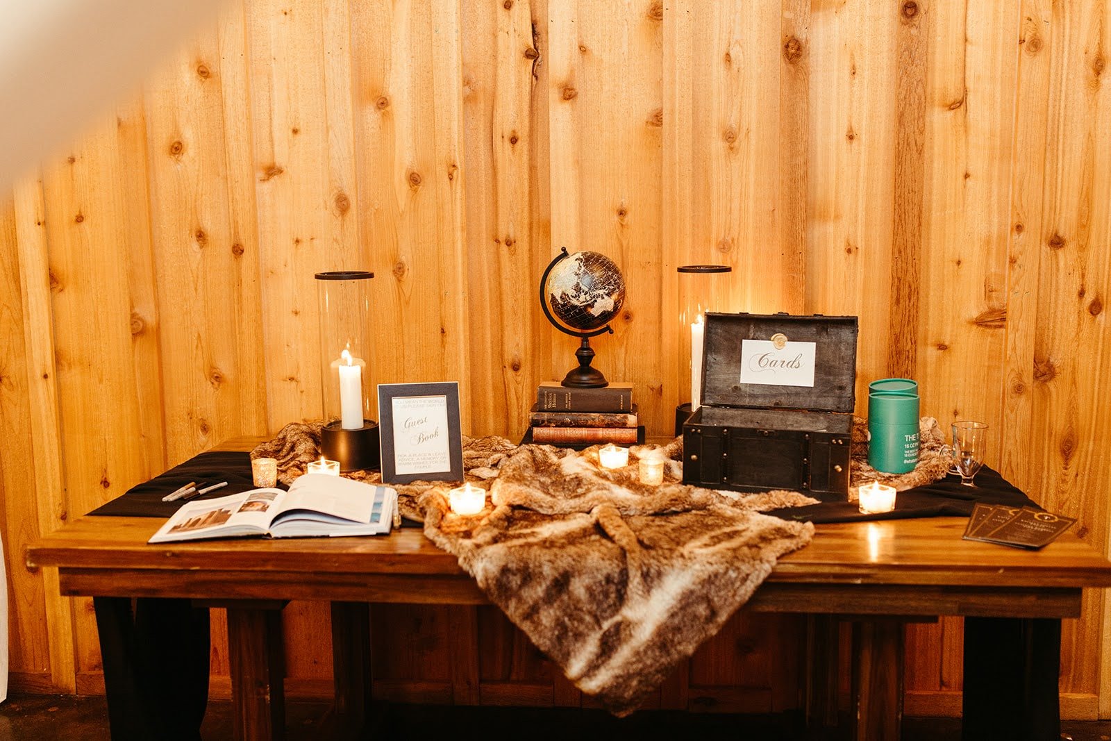 Guestbook table display with candles, framed signs, and decor arranged on a wooden table against a wood-paneled wall.