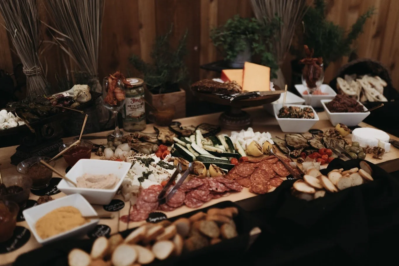 Rustic wedding reception grazing table with charcuterie, bread, fruit, greenery, and candlelight.