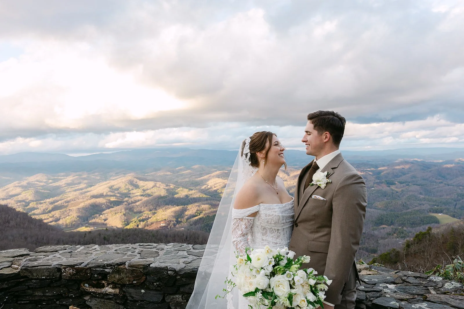 Bride and groom smiling together in front of a sweeping Blue Ridge mountain view after their wedding ceremony.