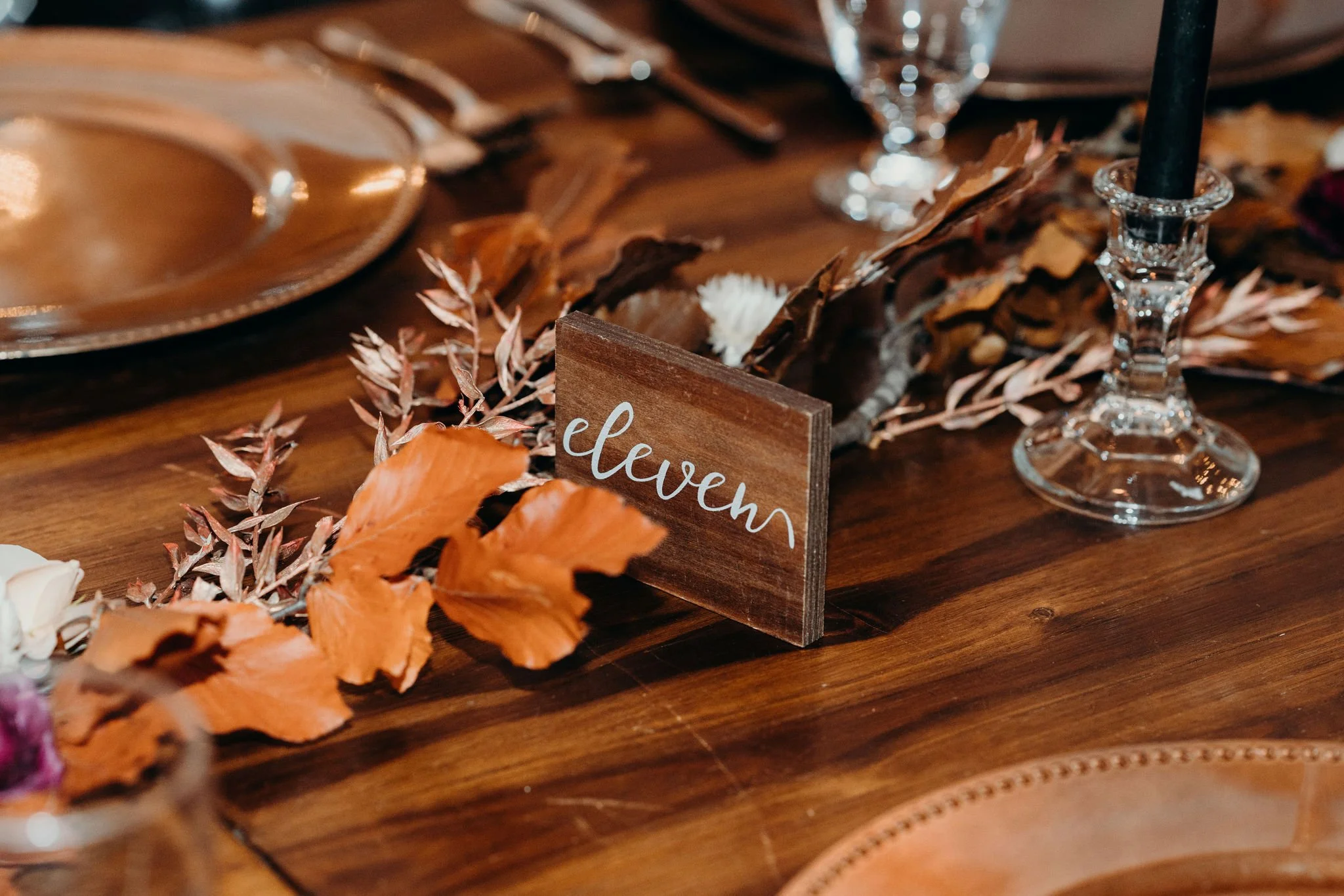 Reception table detail with a wooden table number eleven and fall leaves on a wooden tablescape.