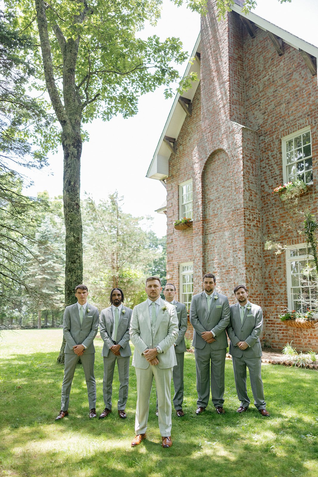 Groom and groomsmen in gray suits posing outside a brick estate wedding venue.