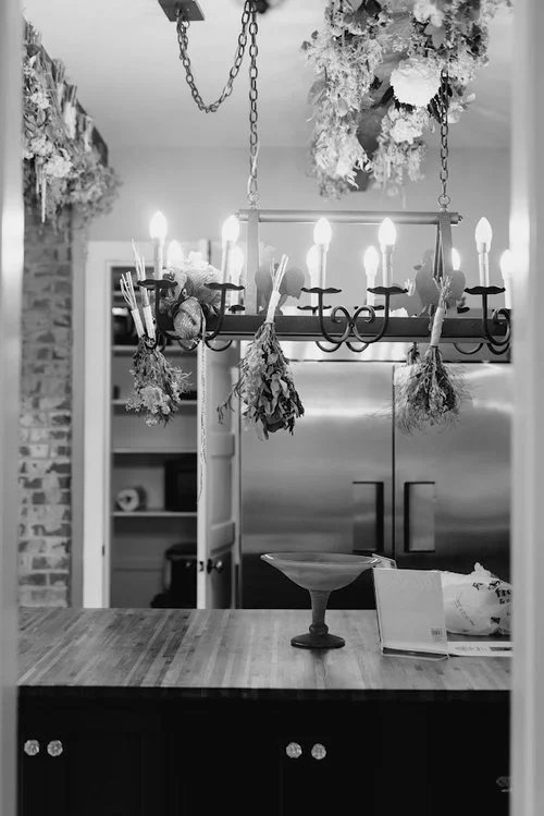Chandelier decorated with dried florals above a kitchen island in a wedding reception space