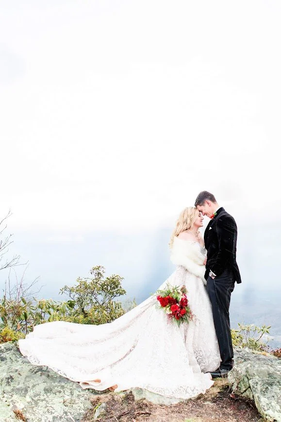 Bride and groom kissing in a forest clearing with sunlight streaming through the trees