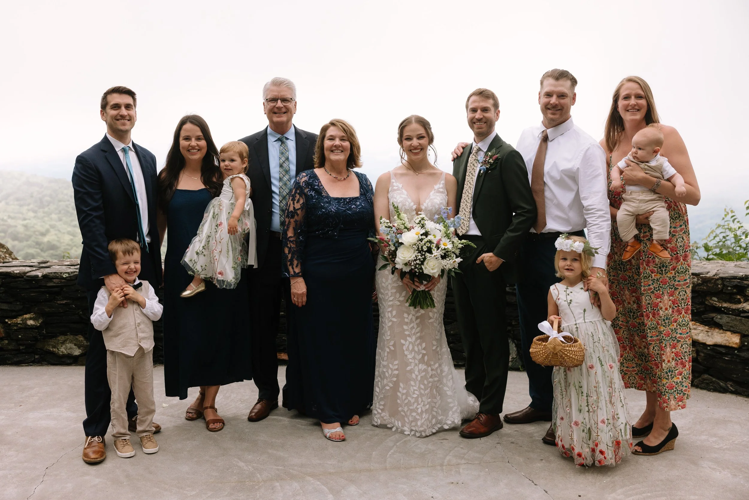 Bride and groom posing with family for a wedding portrait at a misty mountain overlook.