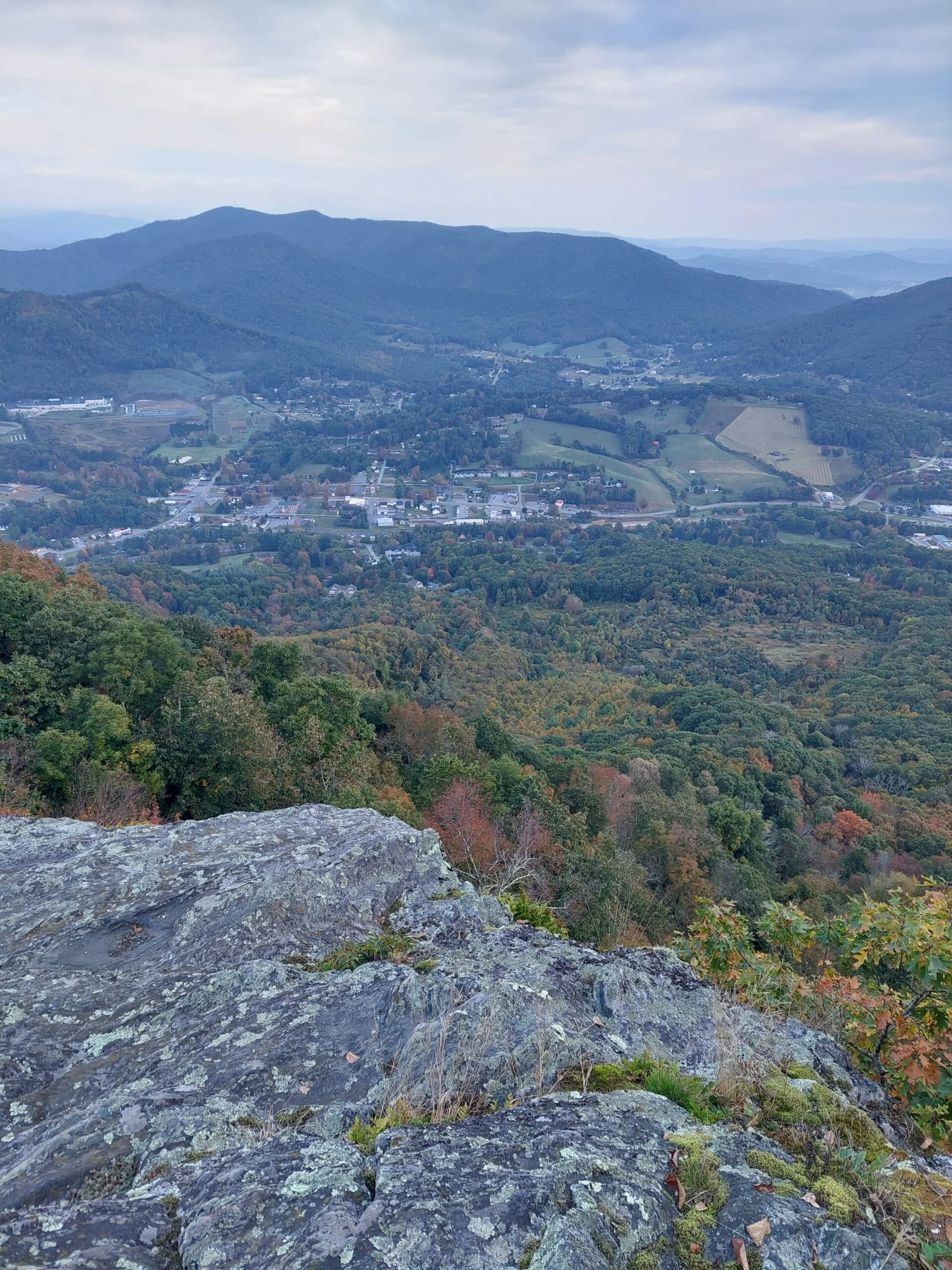 Panoramic mountain overlook with a valley town below and layered ridges in the distance.