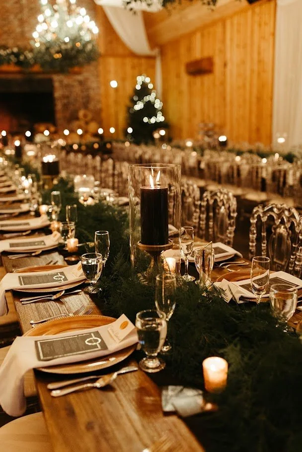 Reception tablescape with greenery runner and candles, with a Christmas tree in the background.