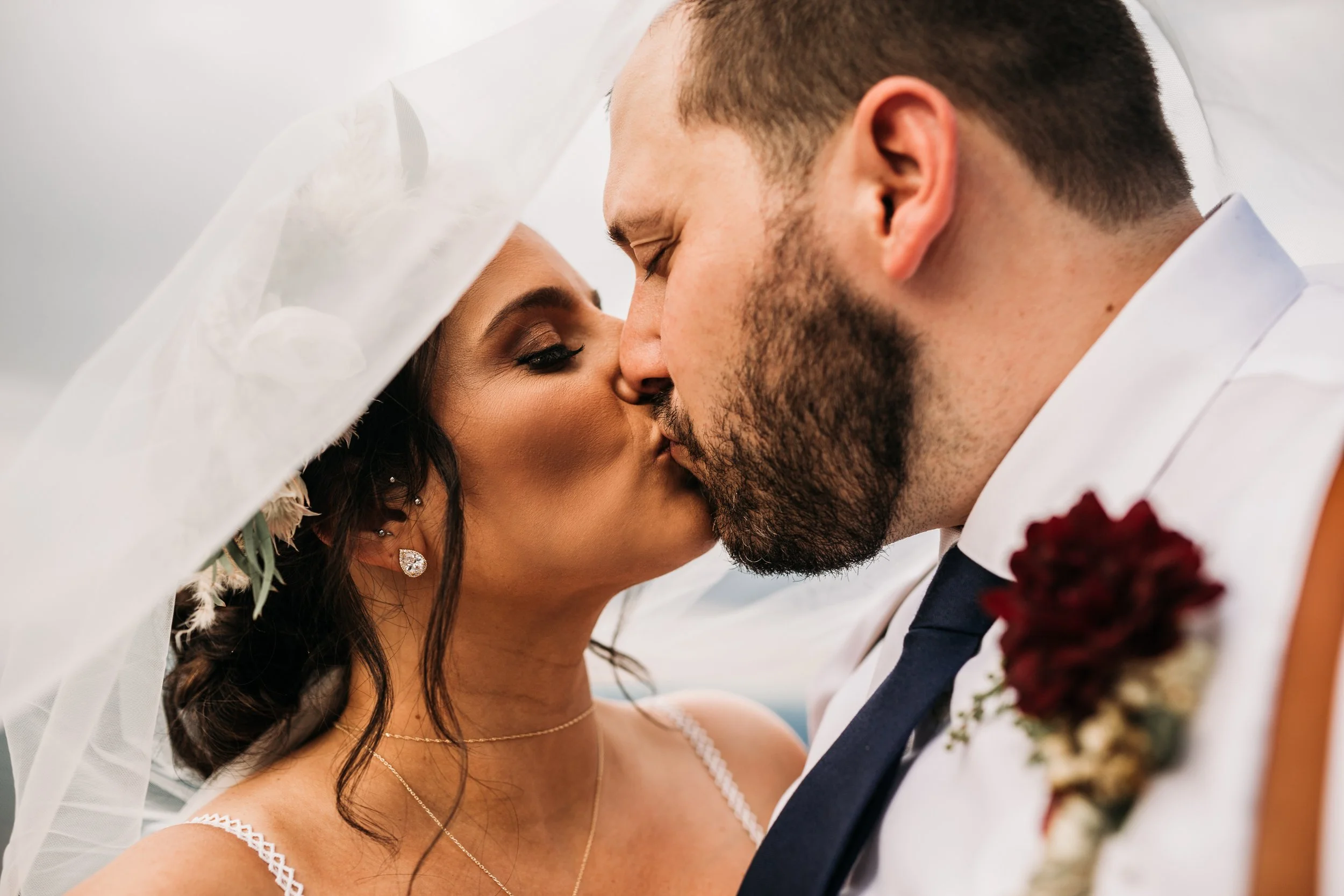 Closeup of the bride and groom kissing with the bride’s veil and the groom’s boutonniere visible.