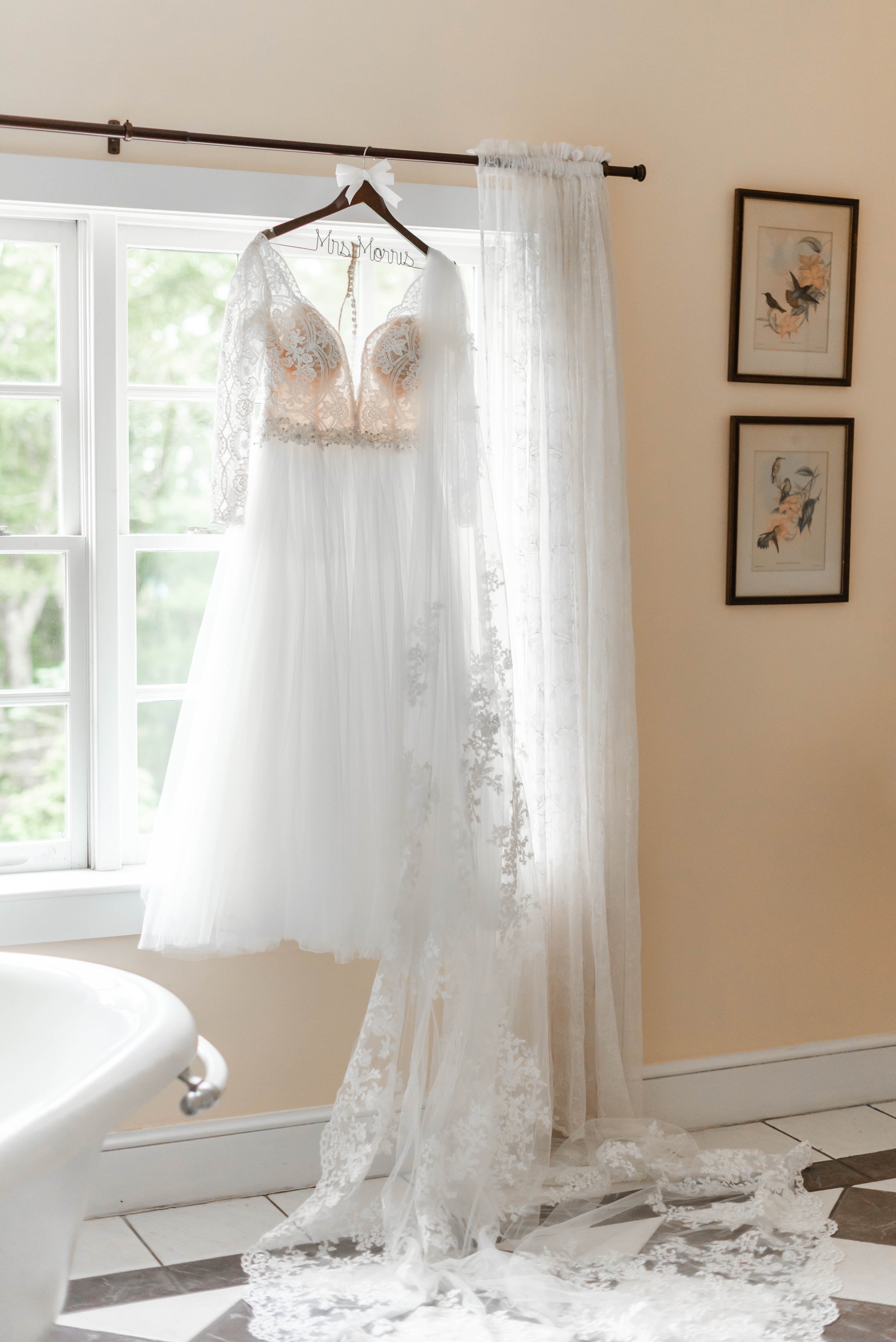 Long sleeve lace wedding dress hanging by a bright window before the ceremony.