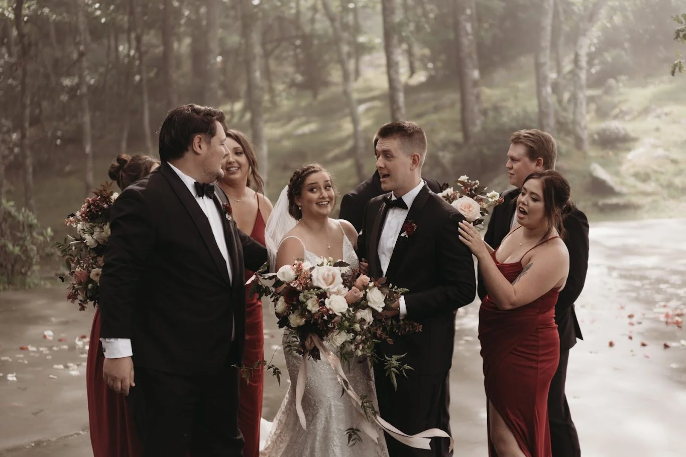 Wedding party laughing together in a forest during group portraits with the bride holding her bouquet