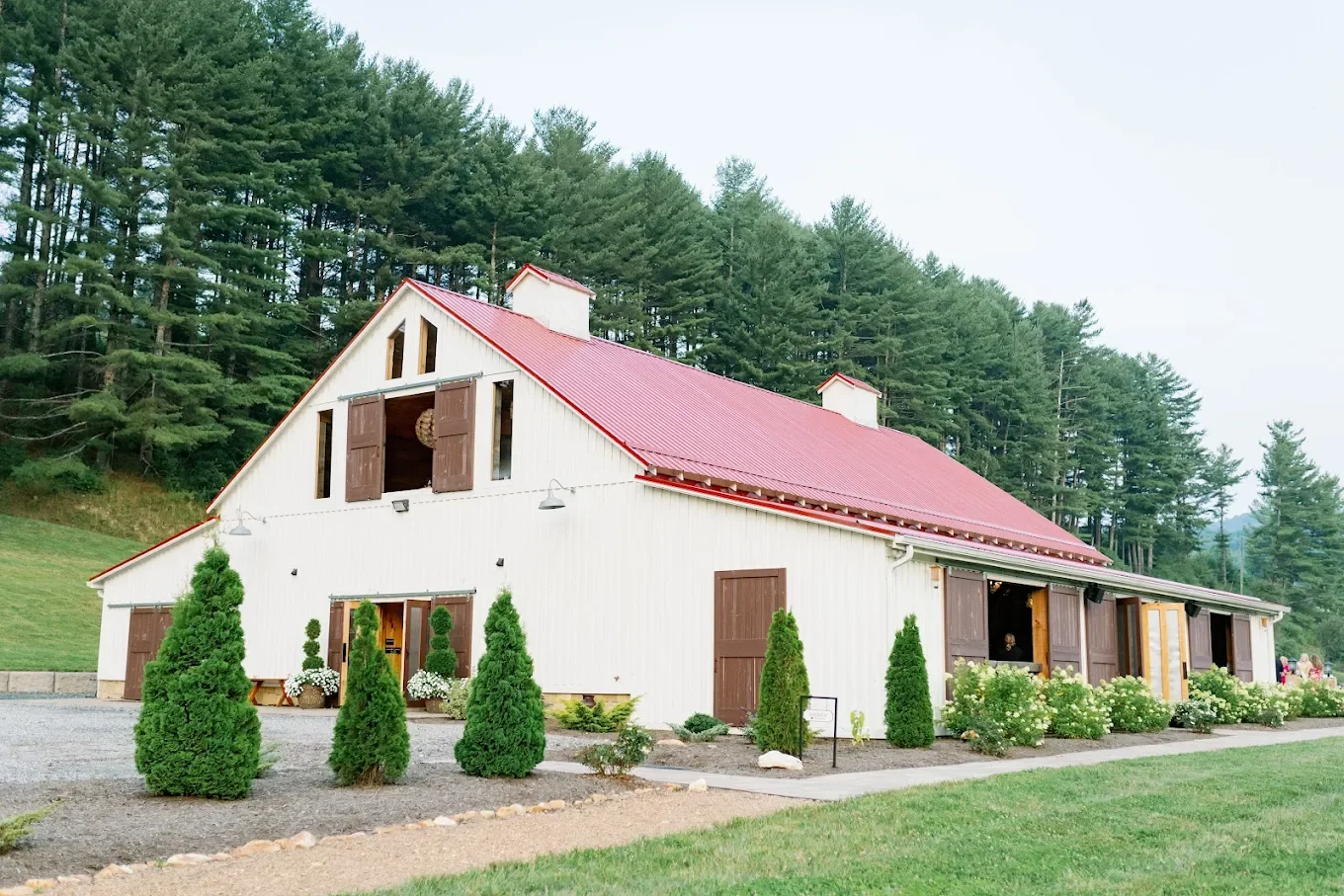 White barn wedding venue with a red metal roof and green pine trees in the background