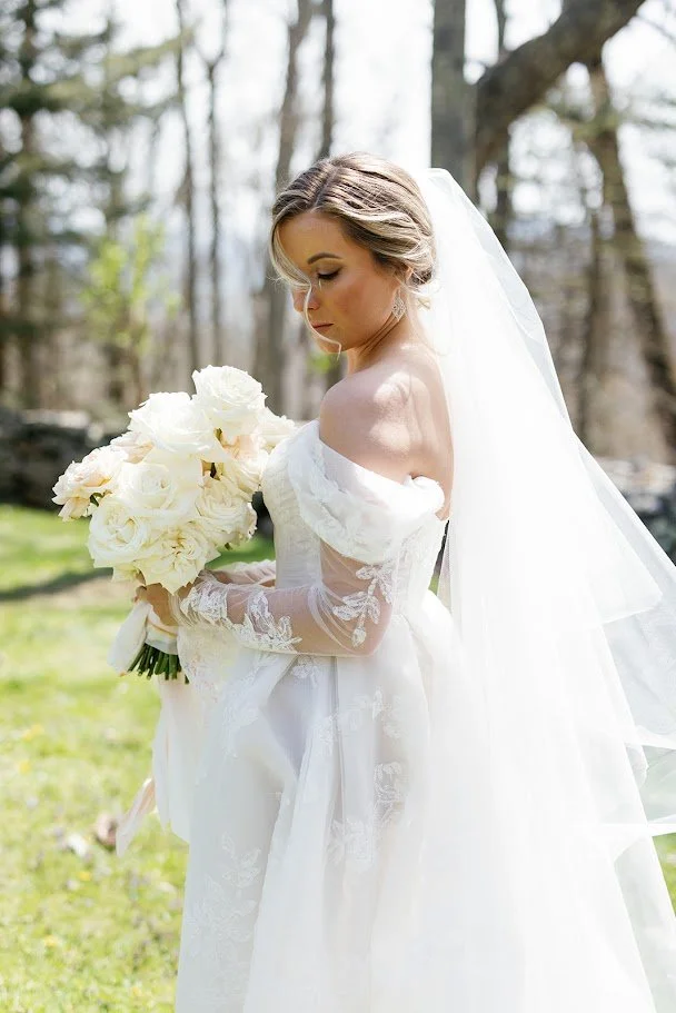 Side-profile bridal portrait showing lace sleeves, veil, and a white rose bouquet