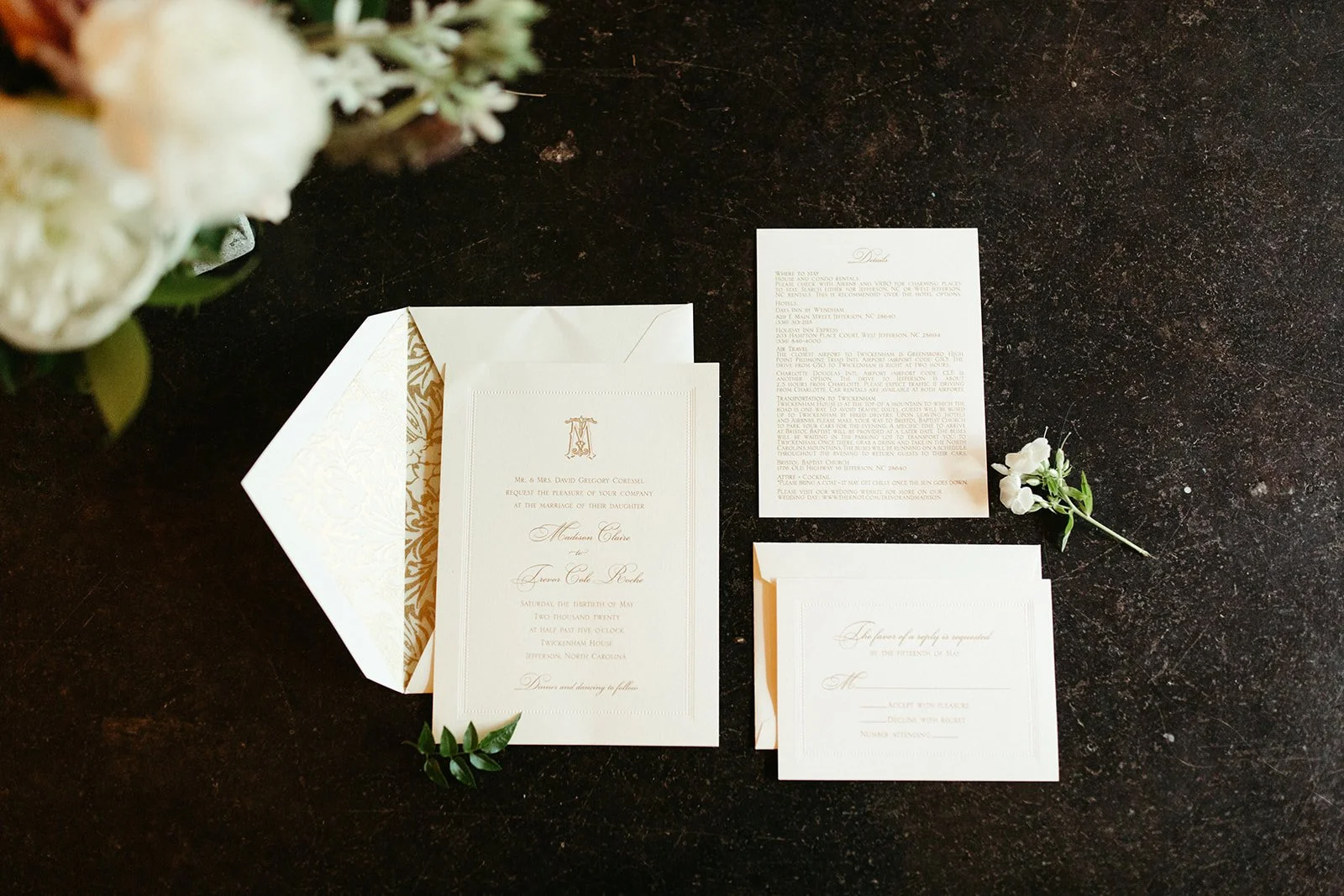 Wedding invitation suite flat lay with envelope, vow cards, and a boutonniere on a dark surface.