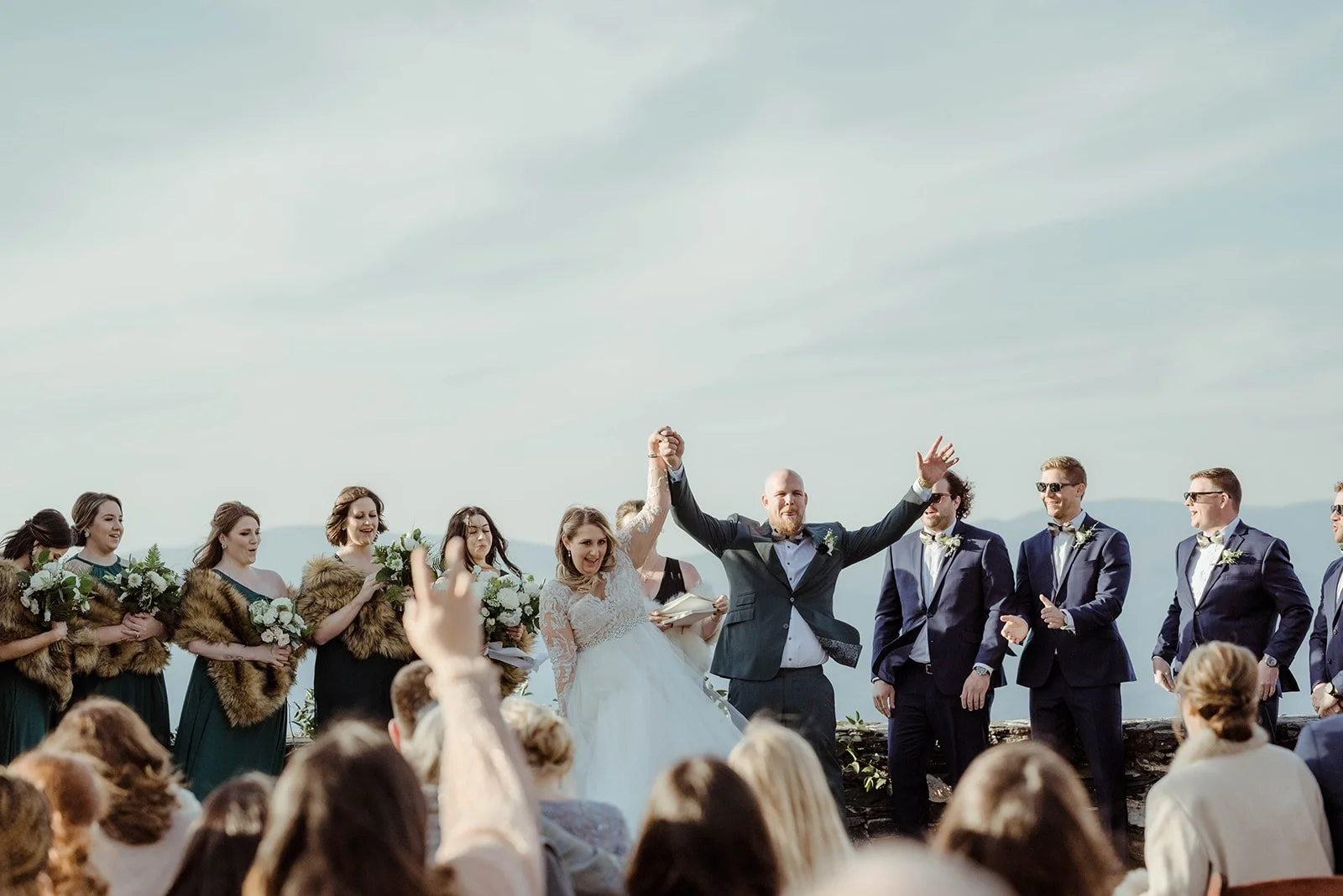 Bride and groom celebrating at the end of an outdoor ceremony with the wedding party behind them on a mountain overlook