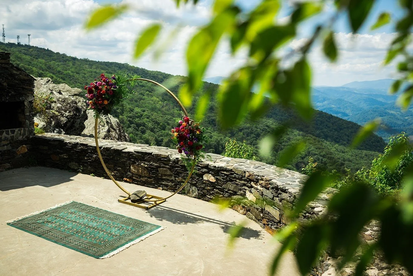 Mountain wedding ceremony terrace with a circular floral arch framed by green leaves in the foreground