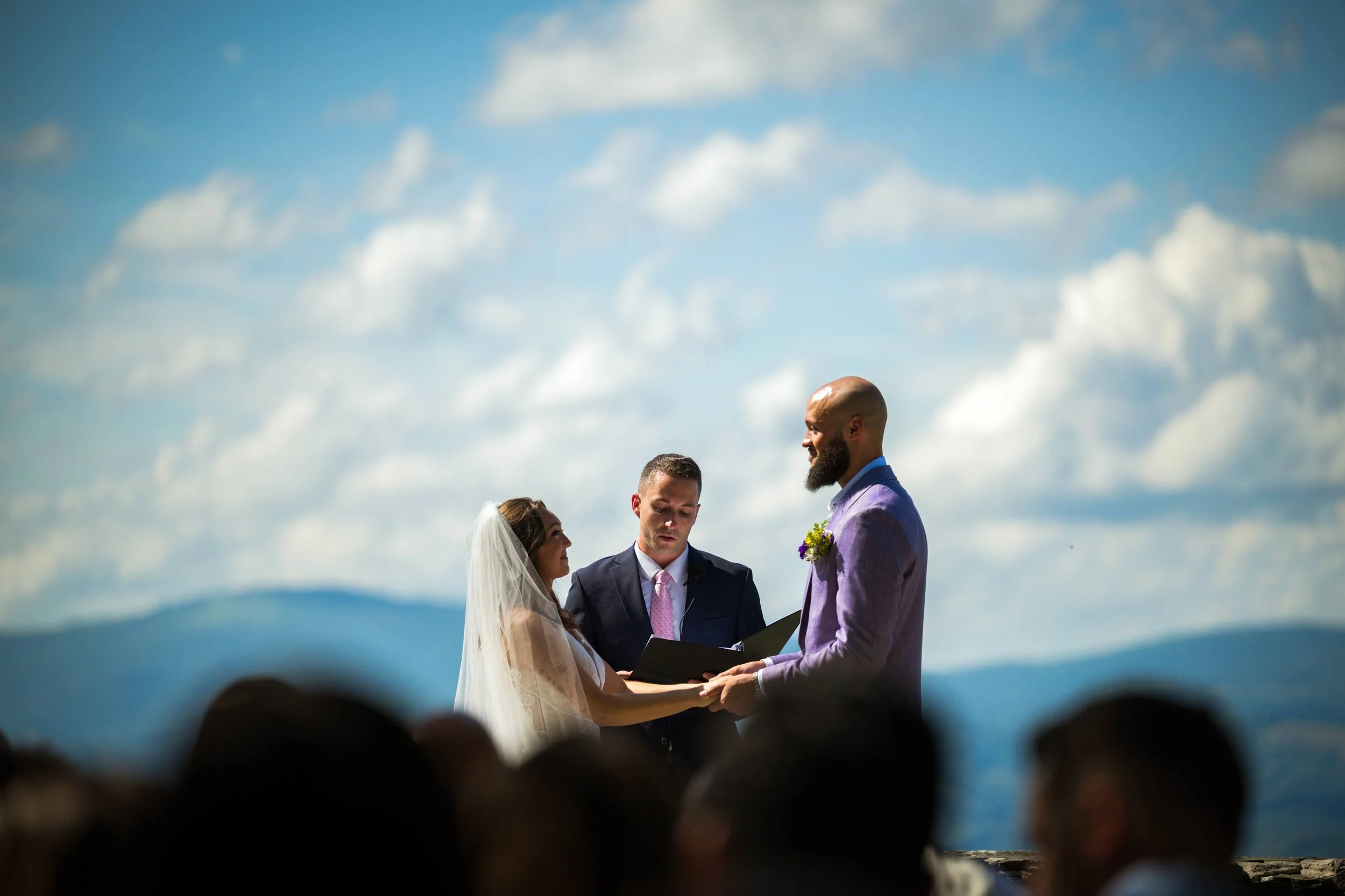 Bride and groom exchanging vows during an intimate outdoor mountain wedding ceremony with officiant and cloudy sky backdrop