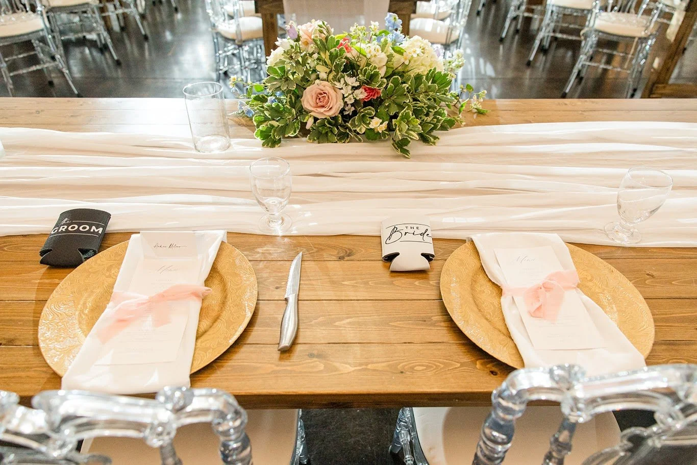 Sweetheart table place settings with gold chargers, blush ribbon napkins, and a floral centerpiece