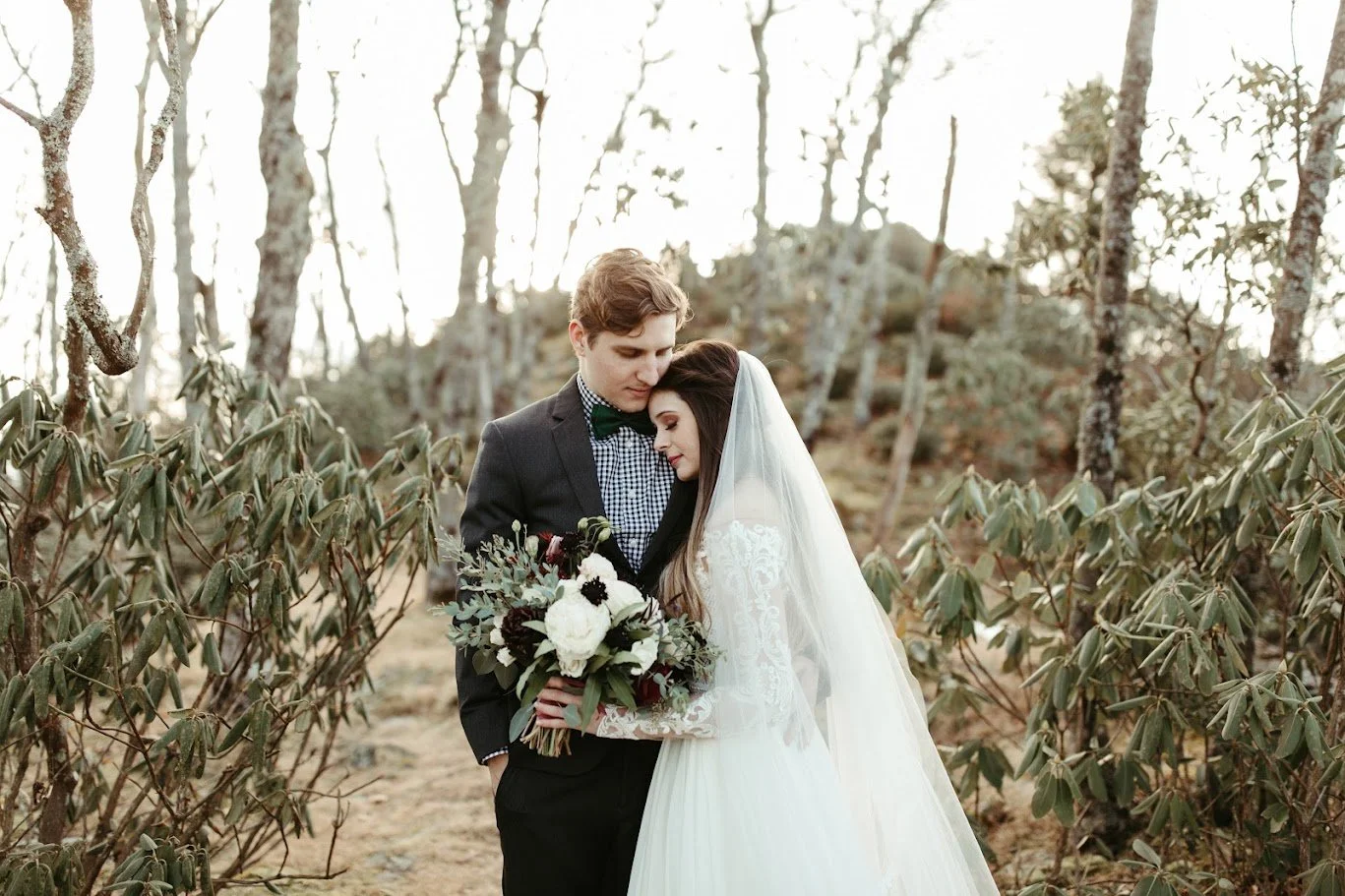 Bride and groom embracing in a wooded mountain setting for a romantic wedding portrait.