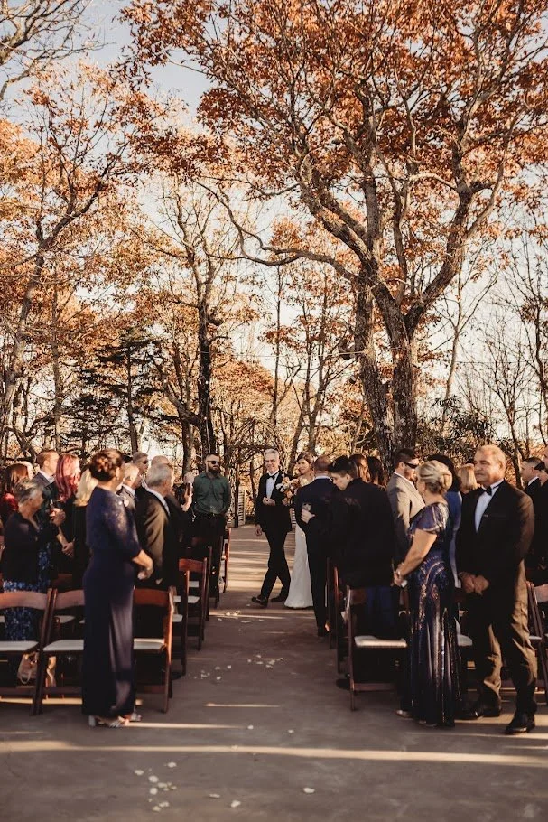 Couple walking down the aisle during an outdoor fall wedding ceremony as guests stand on both sides