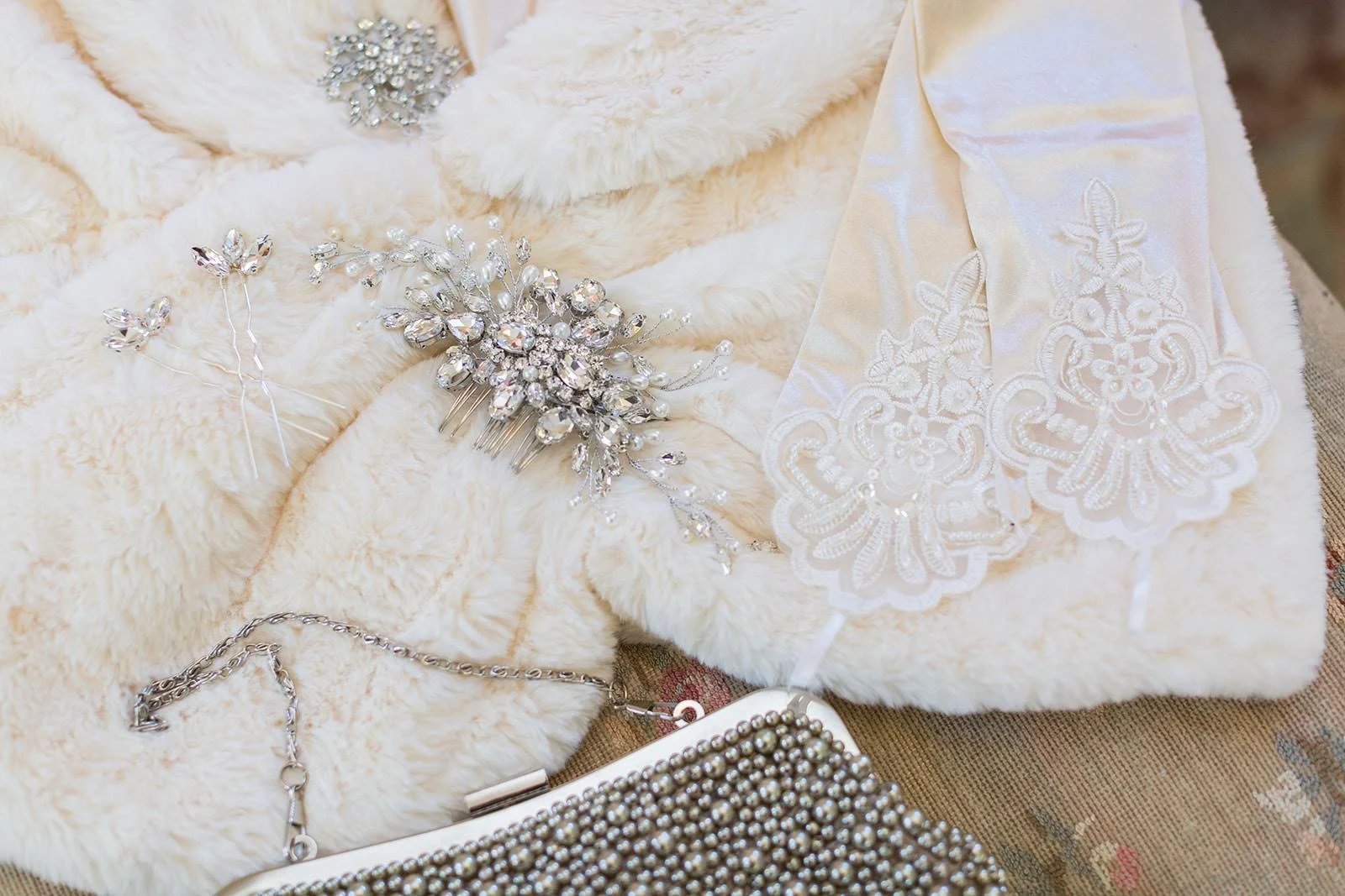 Bridal accessories flat lay featuring a fur wrap, sparkling jewelry, and a rhinestone clutch.
