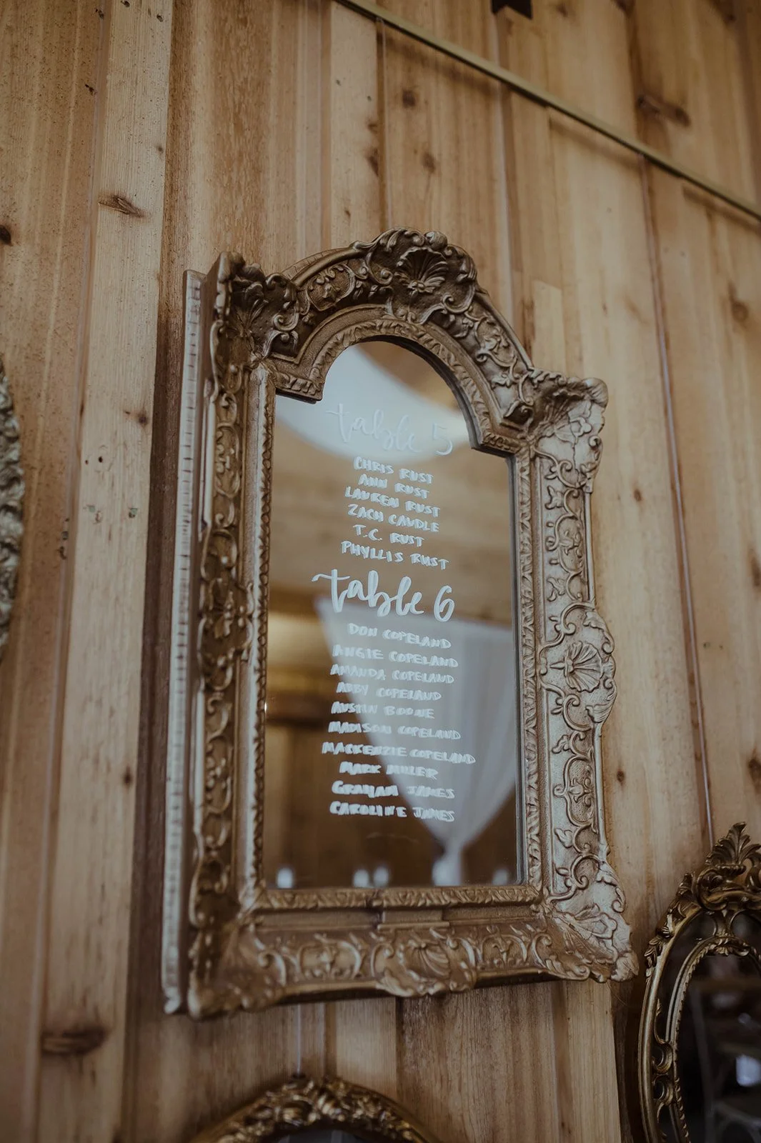Wedding seating chart written on a vintage mirror hanging on a wood wall inside a rustic venue.