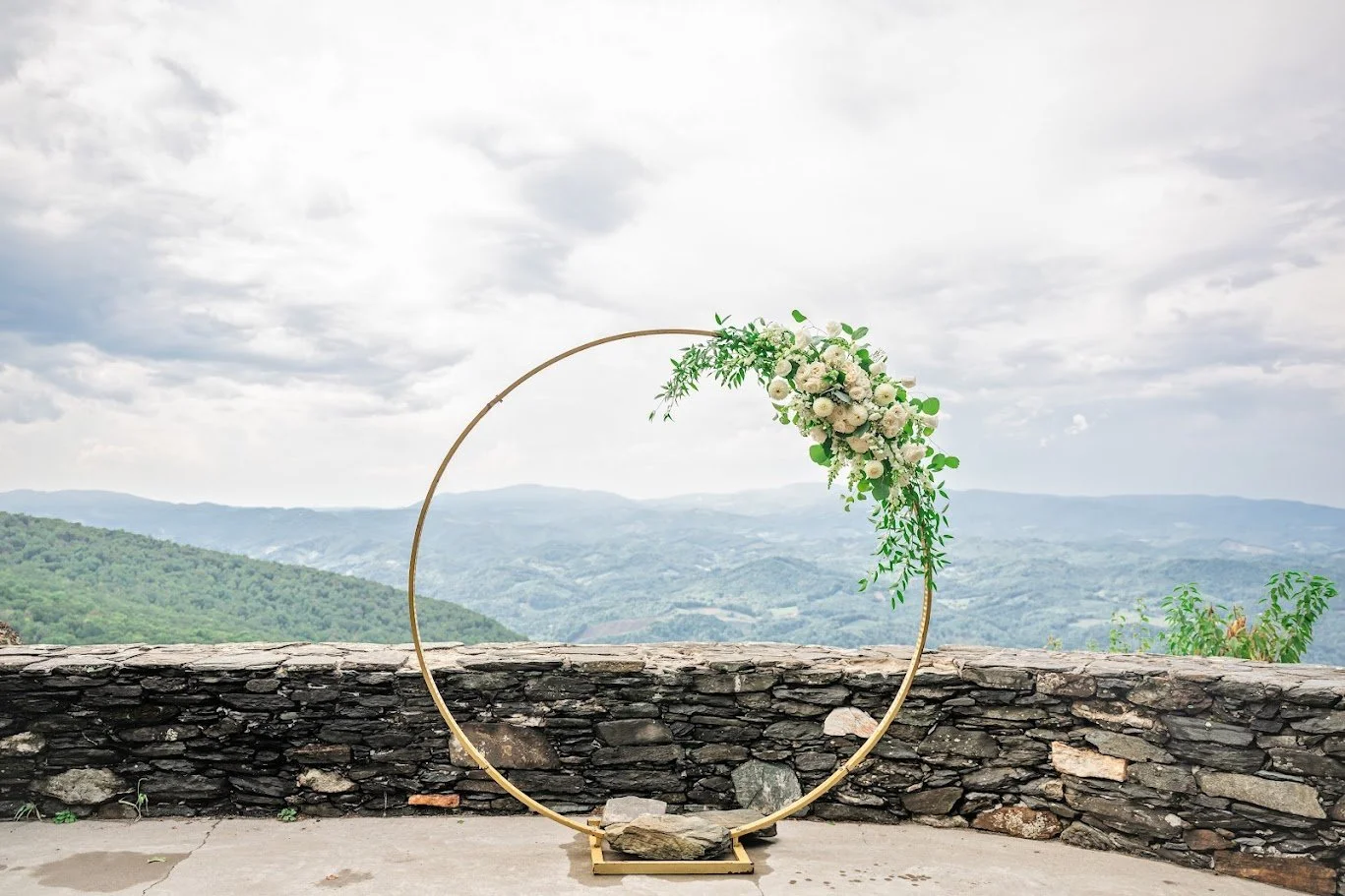 Circular wedding arch with white flowers and greenery on a stone terrace overlooking mountains