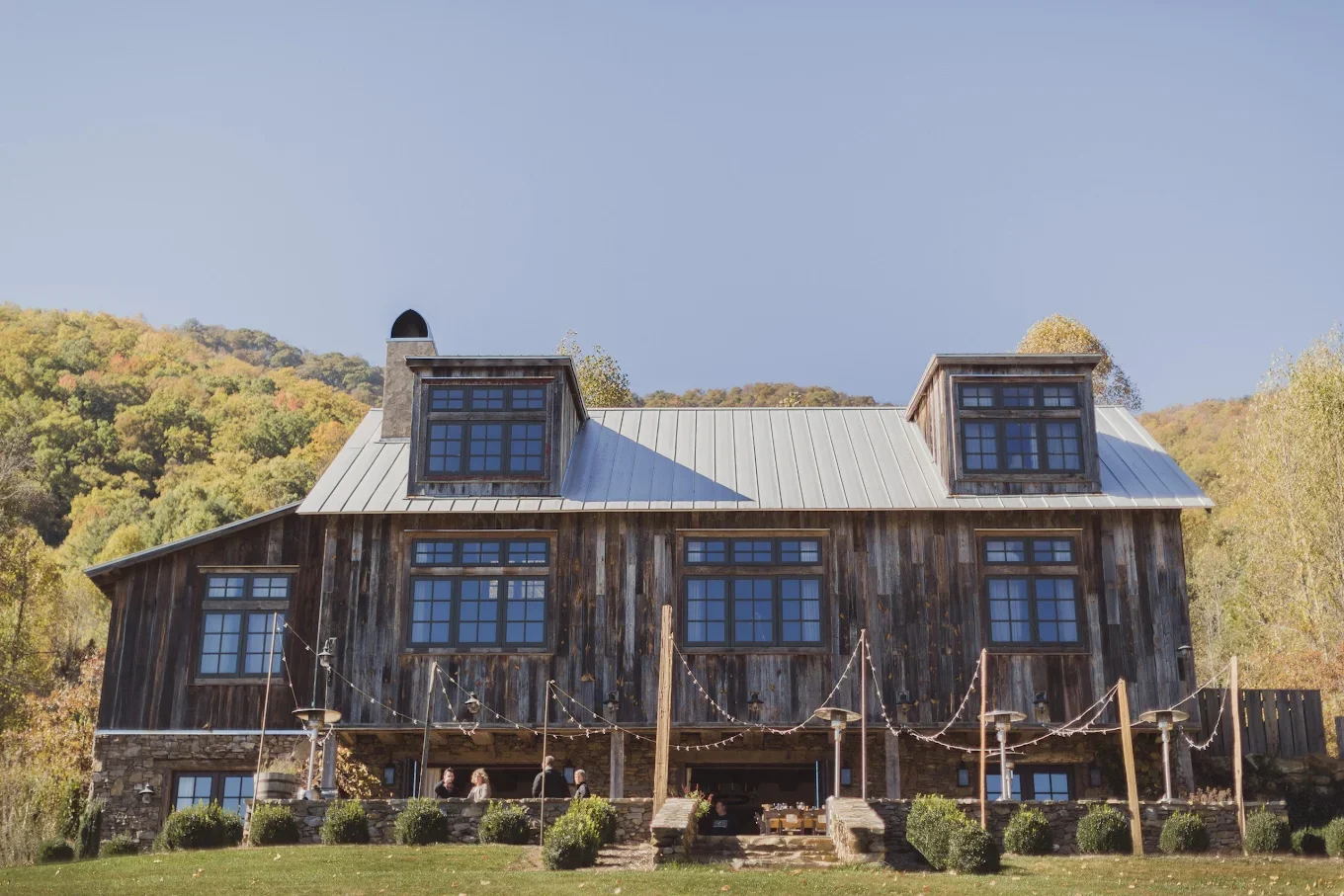 Rustic wooden barn wedding venue exterior with large windows and string lights in a mountain setting
