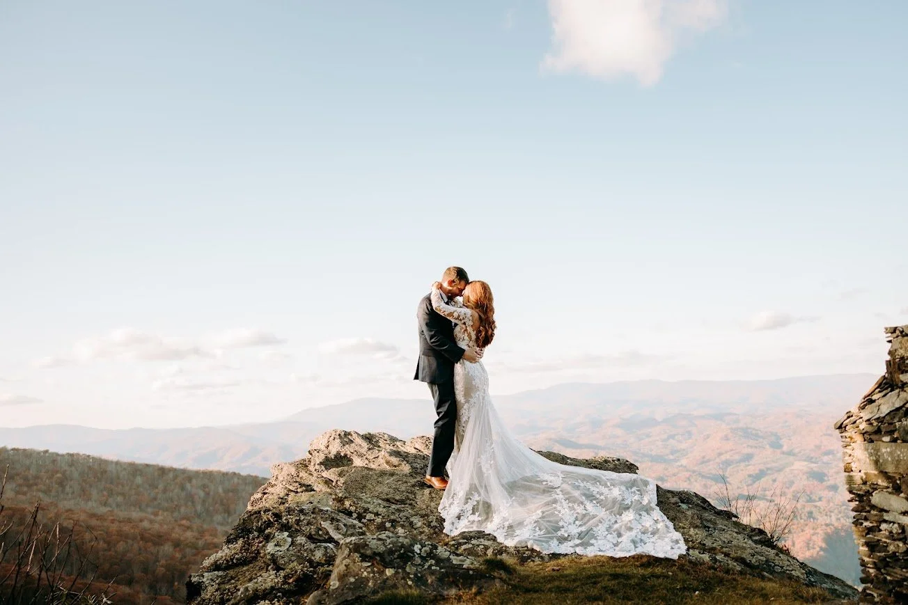 Bride and groom embracing on a rocky overlook with sweeping mountain views