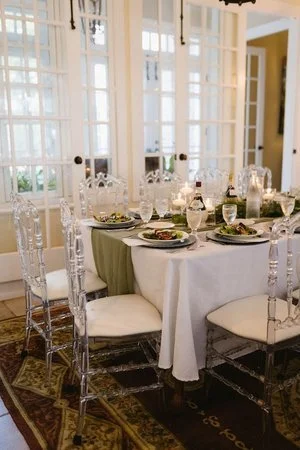 An elegantly set table with white tablecloth, green runner, crystal glasses, candles, and plates of salad, in a bright room with white doors.