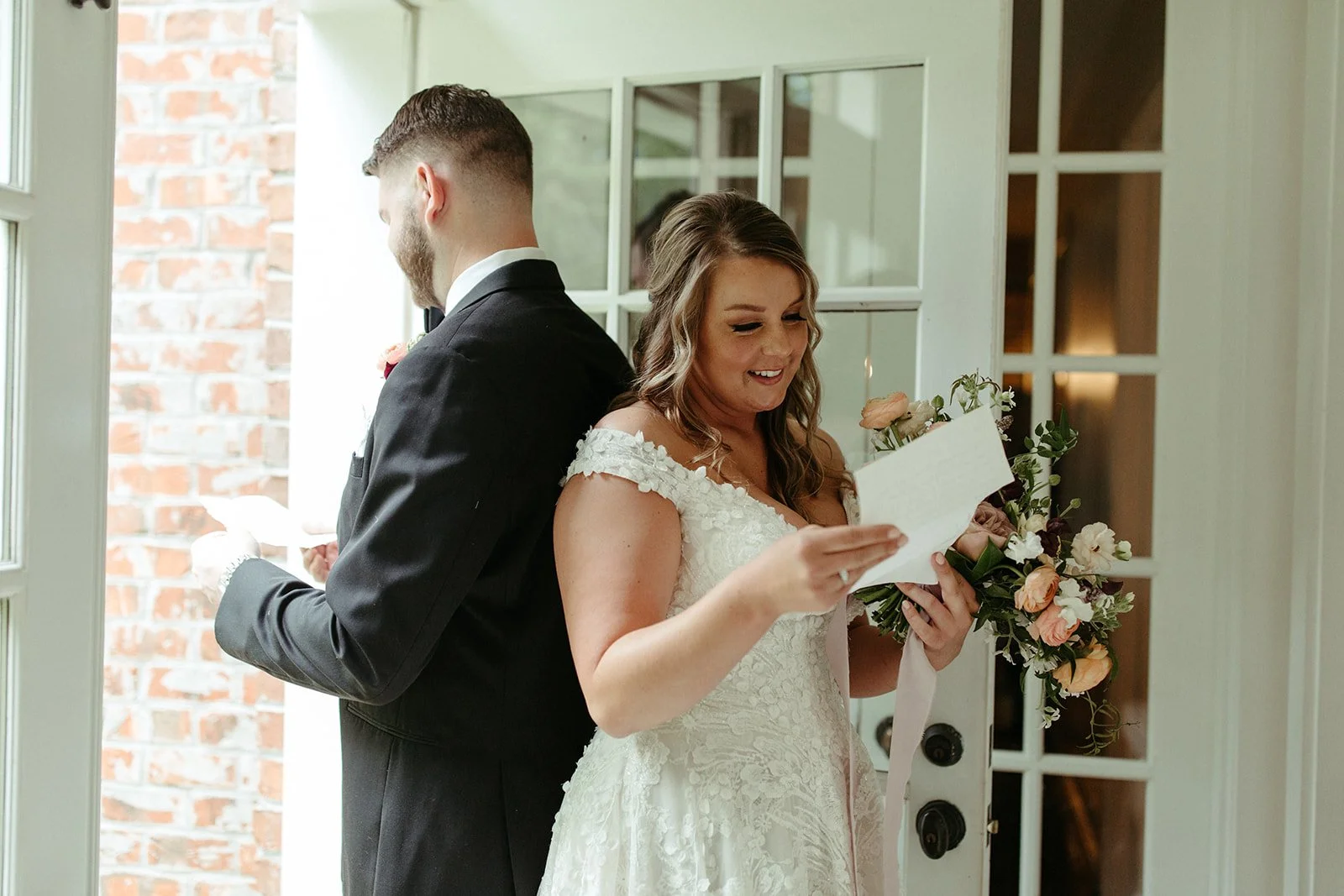 Bride reading a letter while standing back to back with the groom during a first look.