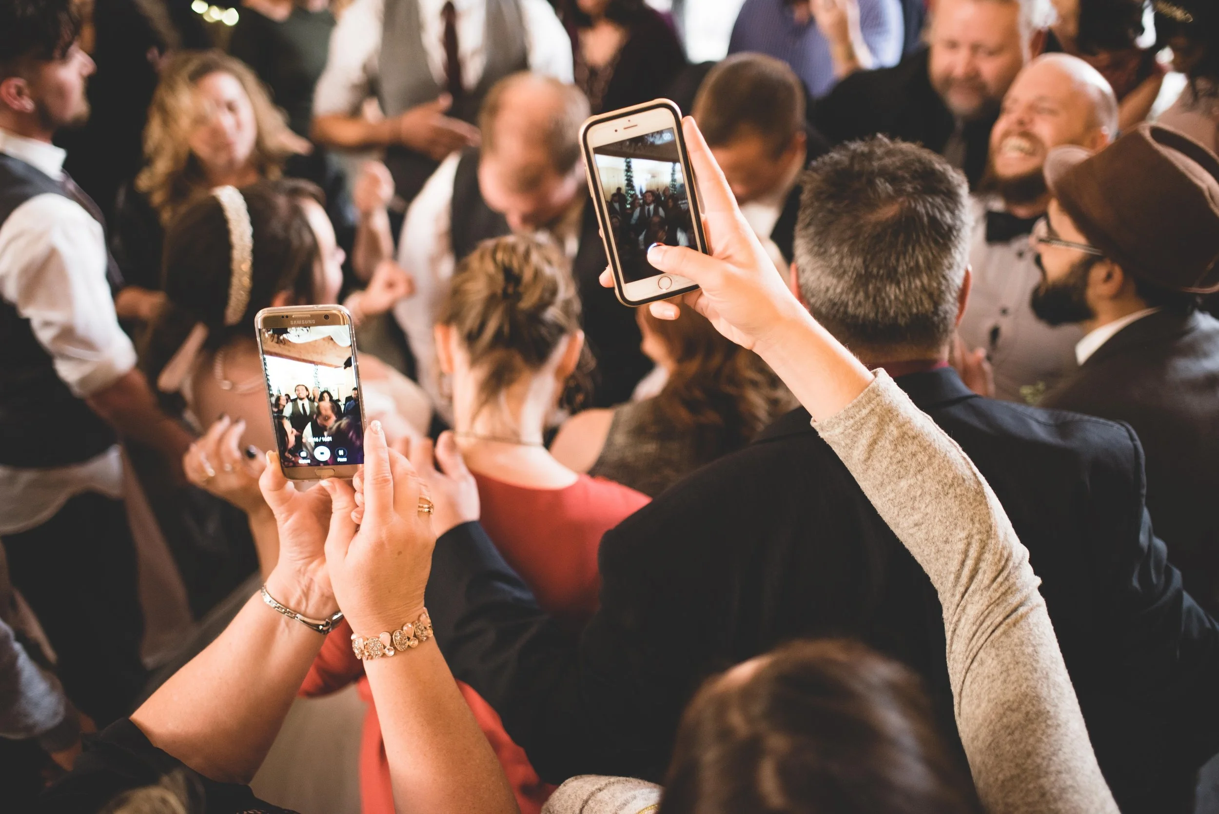 Wedding guests in a crowd holding up smartphones to record the dance floor during the reception.